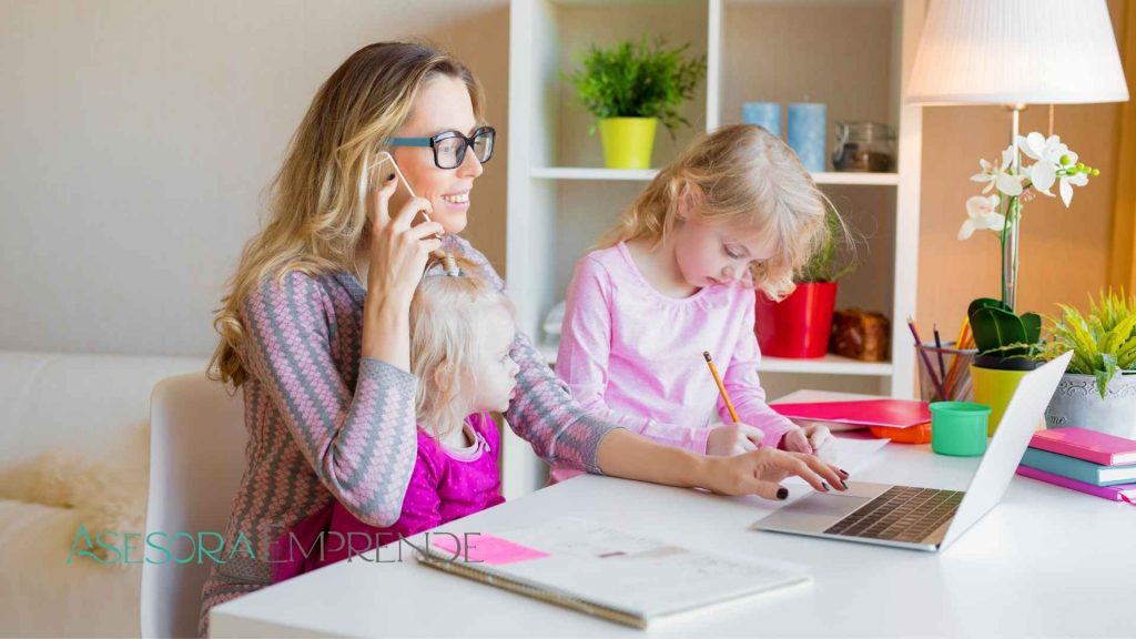 Madre autónoma trabajando desde casa con sus hijas mientras consulta online las 2 semanas más de permiso por nacimiento en el portátil.