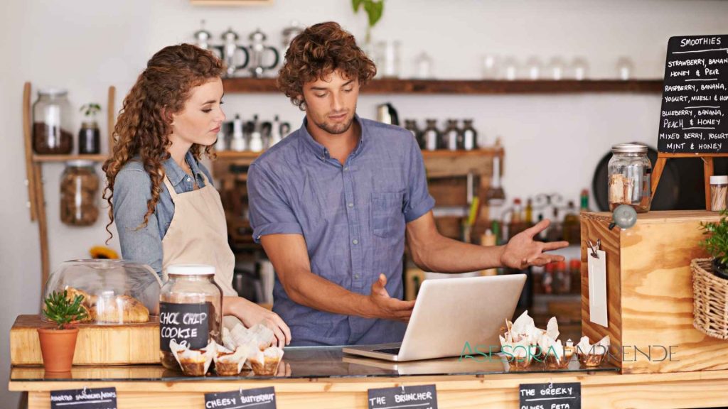 Dos emprendedores gestionando una pequeña empresa en su negocio, revisando el ordenador para conocer los tipos reducidos para pequeñas sociedades en 2025